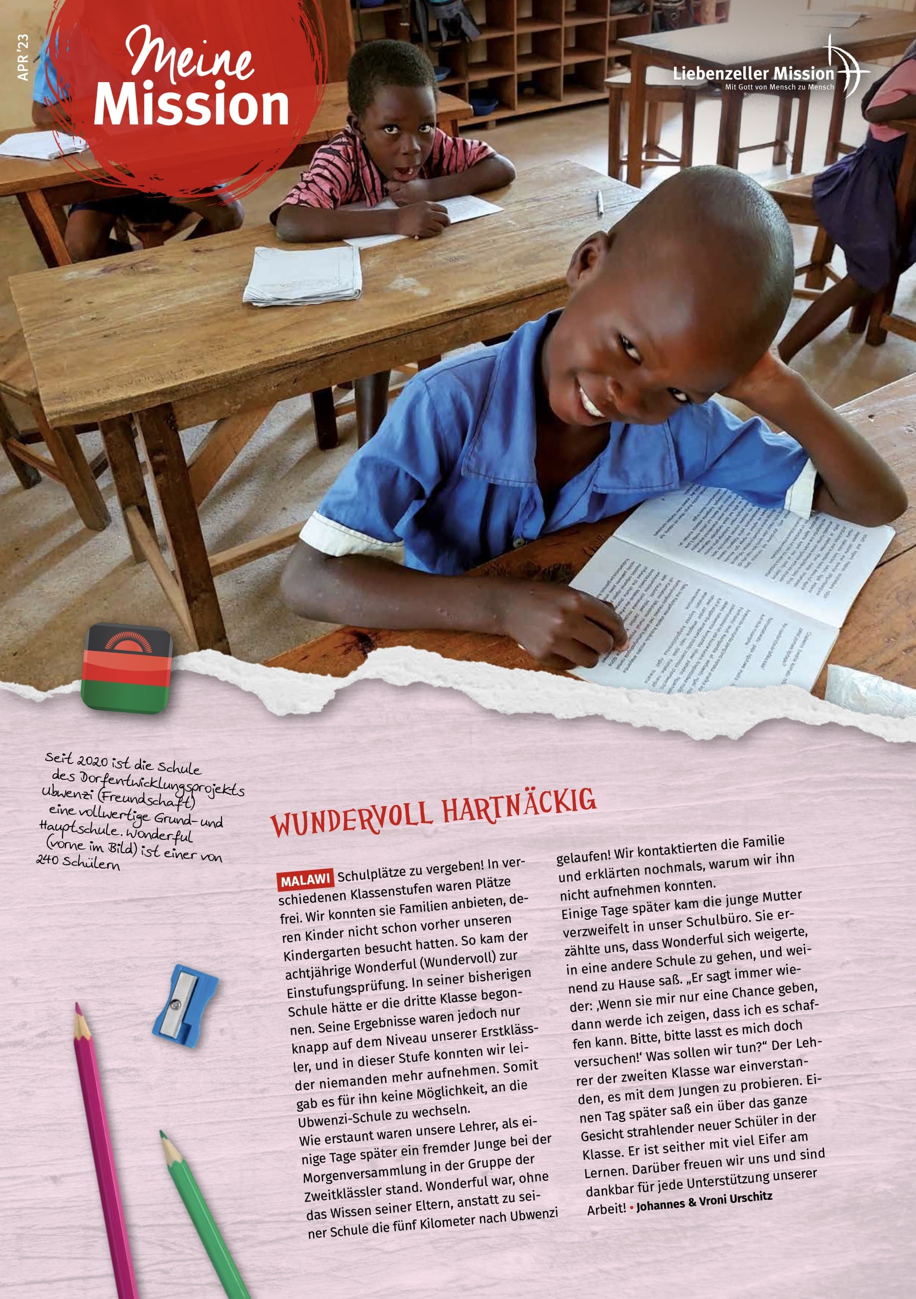 Ein lächelnder Junge sitzt an einem hölzernen Schreibtisch in einem Klassenzimmer und schreibt "Meine Mission" in sein Notizbuch, April 2023.