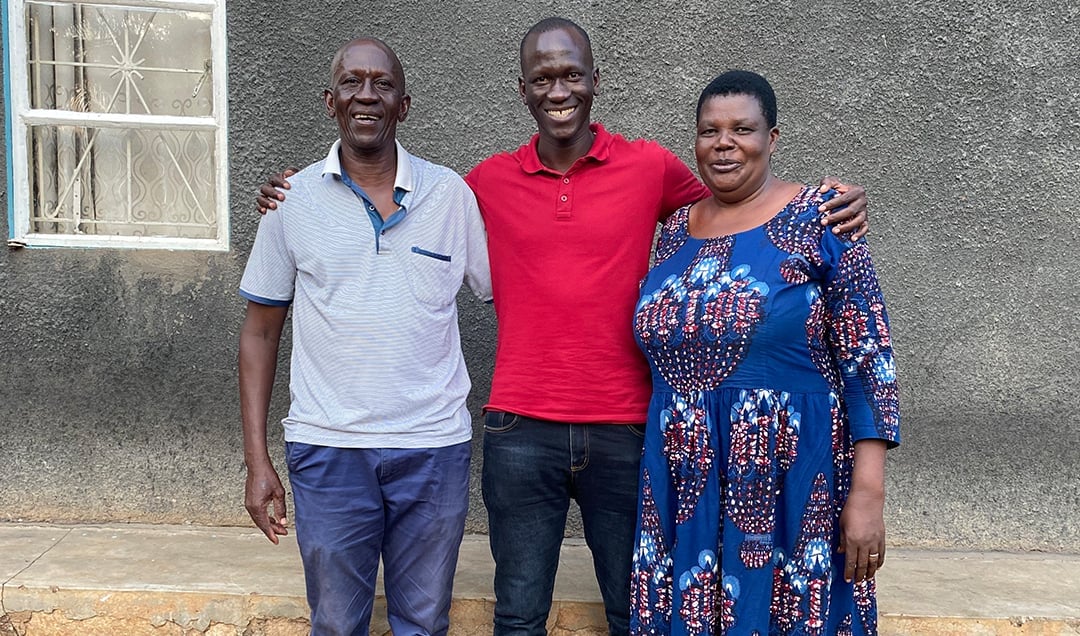 Drei Menschen stehen lächelnd, Arm in Arm, vor einer grauen Wand.