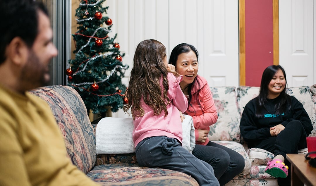 Vier Menschen plaudern und lachen in einer gemütlichen Wohnstube neben einem Weihnachtsbaum.