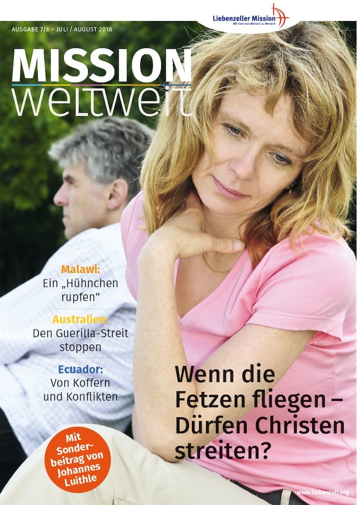 Eine nachdenkliche Frau sitzt im Freien und stützt ihren Kopf auf ihre Hand, während ein Mann im Hintergrund verschwommen zu sehen ist.