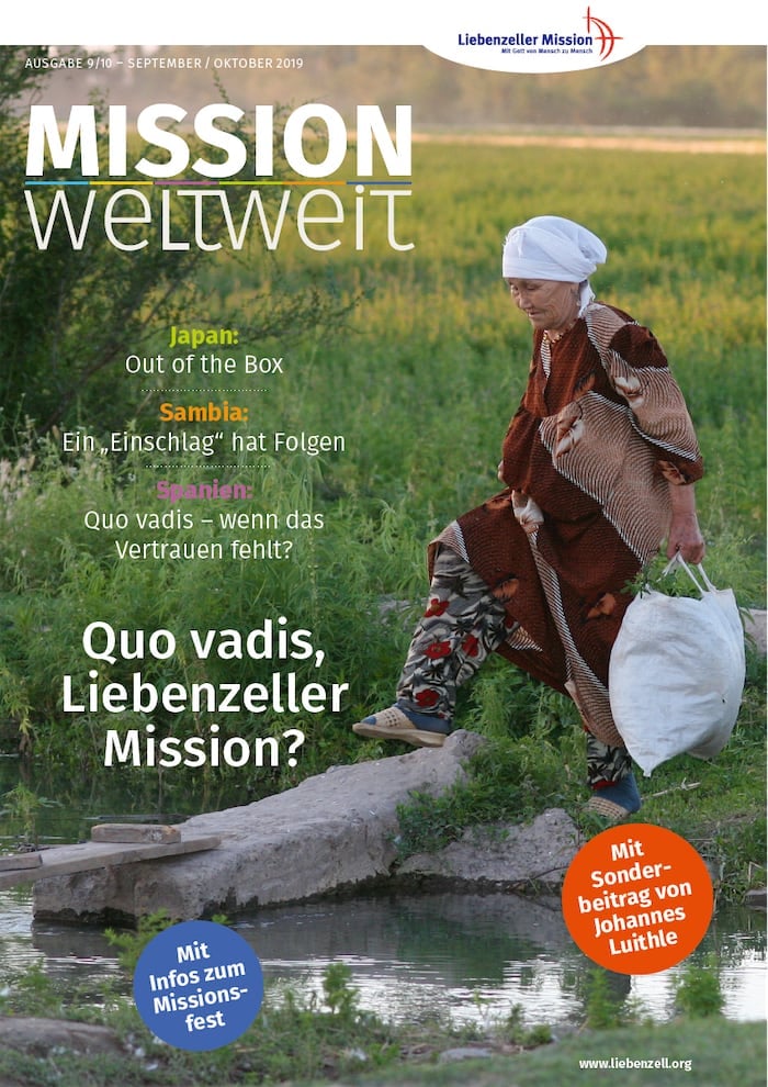 Ältere Frau in traditioneller Kleidung trägt einen Eimer an einem kleinen Teich; Titelbild einer Zeitschrift mit deutschem Text.