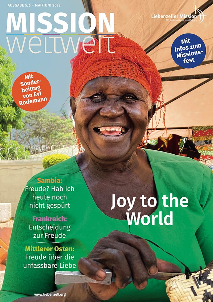 Eine ältere Frau in farbenfroher Kleidung und mit Kopftuch lächelt breit, eine Tasse in der Hand, auf dem Cover einer Zeitschrift mit dem Titel MISSION weltweit.