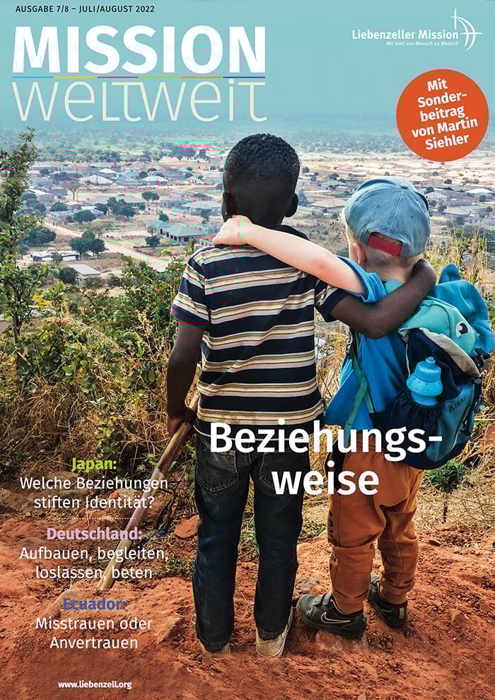 Zwei Jungen, ein Schwarzer und ein Weißer, stehen Arm in Arm und blicken auf ein ländliches Dorf und die Landschaft.