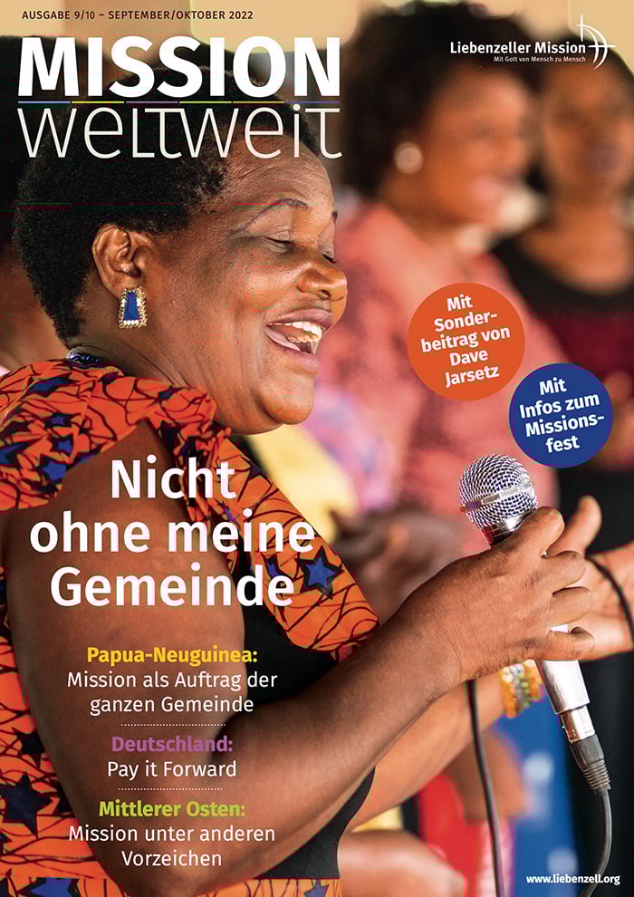 Lächelnde Frau singt während einer Veranstaltung in ein Mikrofon; farbenfrohes Kleid und fröhliche Stimmung.