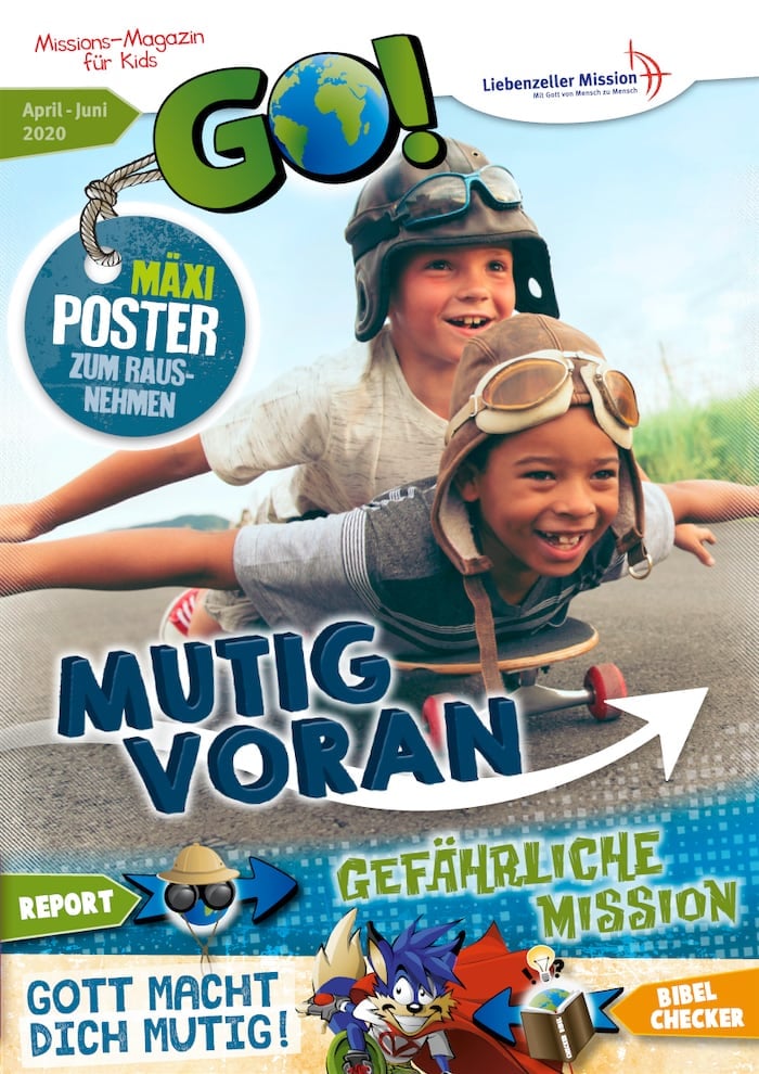 Zwei lächelnde Jungen fahren zusammen auf einem Skateboard auf einer Wiese, der eine liegend, der andere sitzend, beide tragen Helme.