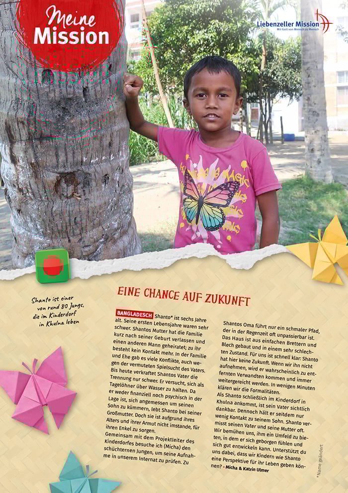 Ein kleiner Junge in einem rosa Schmetterlingshemd steht an einem Baum auf einer Wiese im Freien und lächelt in die Kamera.