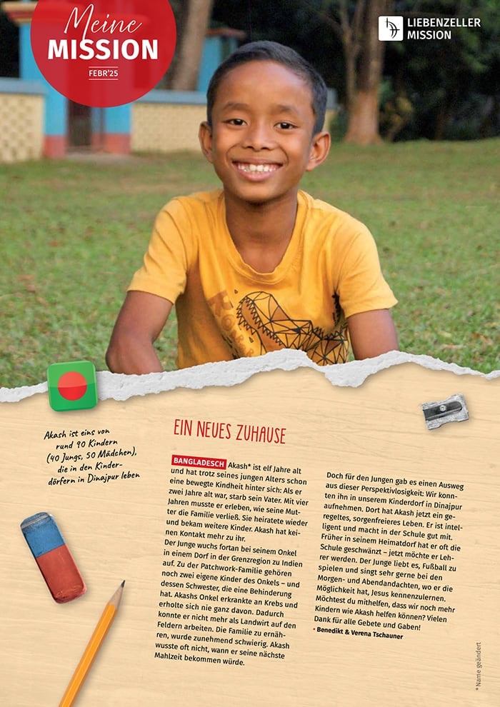 Ein lächelnder Junge in einem gelben Hemd sitzt im Schneidersitz im Gras, im Hintergrund sind ein Gebäude und Bäume zu sehen.