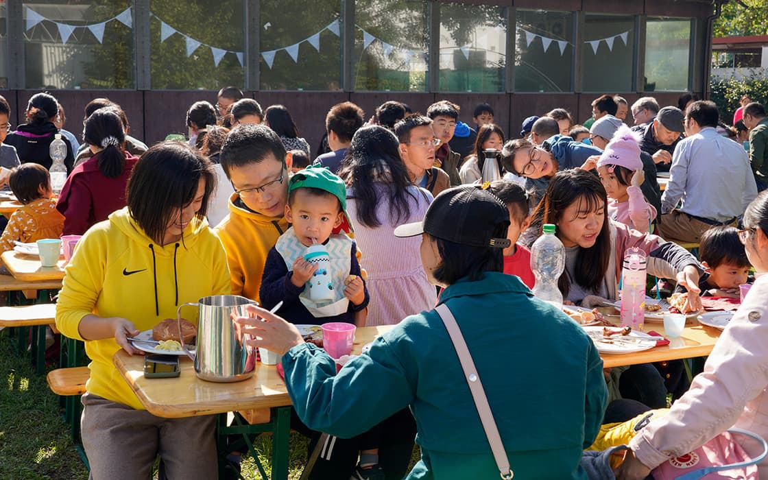 Die Menschen sitzen an Tischen im Freien und essen und trinken gemeinsam in einer lebhaften Gemeinschaft im Sonnenlicht.