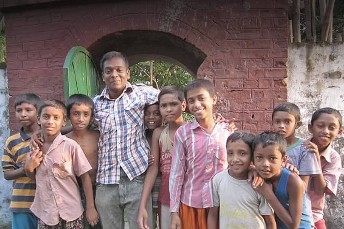 Eine Gruppe lächelnder Jungen posiert gemeinsam im Freien vor einer Backsteinmauer und einer grünen Tür.