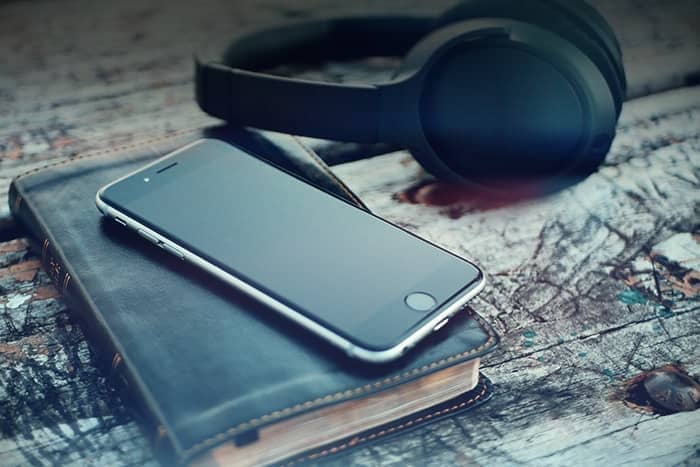 Ein Smartphone, ein geschlossenes Notizbuch und schwarze Kopfhörer auf einer rustikalen Holzoberfläche.