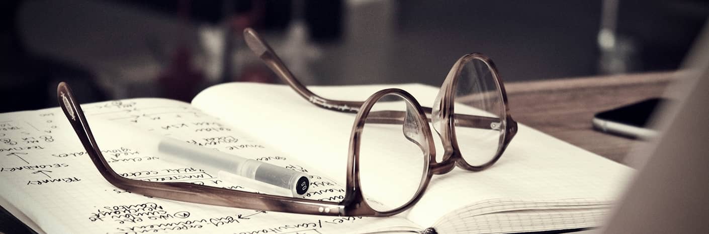 Eine Brille und ein Stift liegen auf einem aufgeschlagenen Notizbuch mit handschriftlichen Notizen.