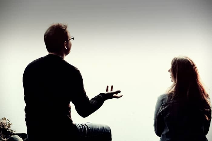 Ein Mann und eine Frau sitzen zusammen und unterhalten sich vor einem hellen, verschwommenen Hintergrund.