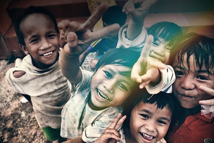 Fünf lächelnde Kinder blicken in die Kamera, machen mit ihren Fingern Friedenszeichen und zeigen freudige Mienen.