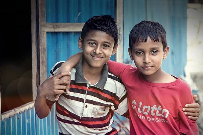 Zwei lächelnde Jungen, die nebeneinander stehen und einen Arm um den anderen legen, vor einer blauen Wand.