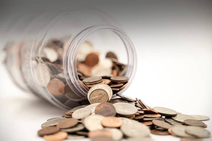 Ein umgekipptes Glas mit verschiedenen Münzen, die auf eine weiße Fläche fielen.