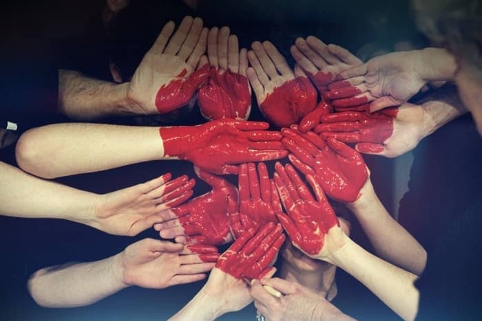 Eine Gruppe rot bemalter Hände bildet vor einem dunklen Hintergrund eine Herzform.
