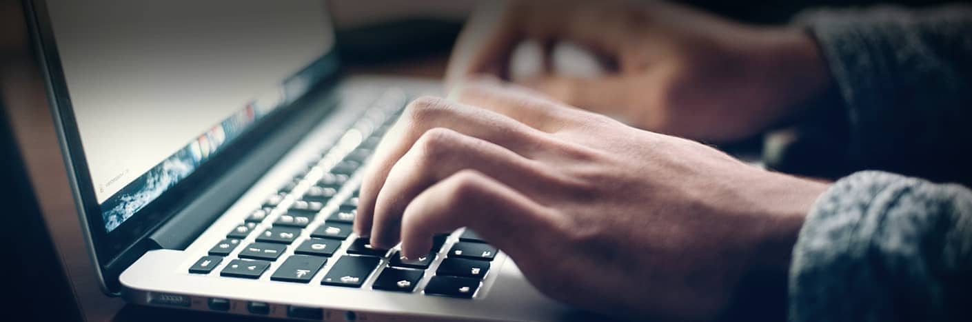 Nahaufnahme von Händen, die auf einer Laptop-Tastatur tippen, mit einem verschwommenen Bildschirm im Hintergrund.