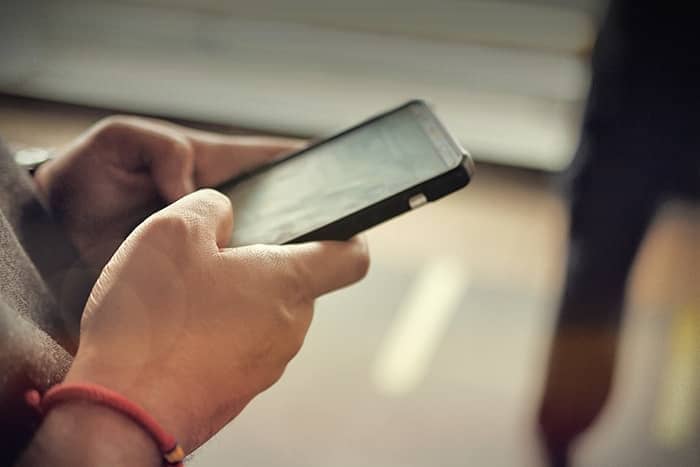 Nahaufnahme von Händen, die ein Smartphone halten und benutzen, mit unscharfem Hintergrund.