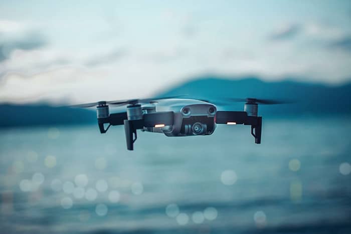 Eine kleine Drohne fliegt über Wasser mit Bergen im Hintergrund, aufgenommen bei Tageslicht.