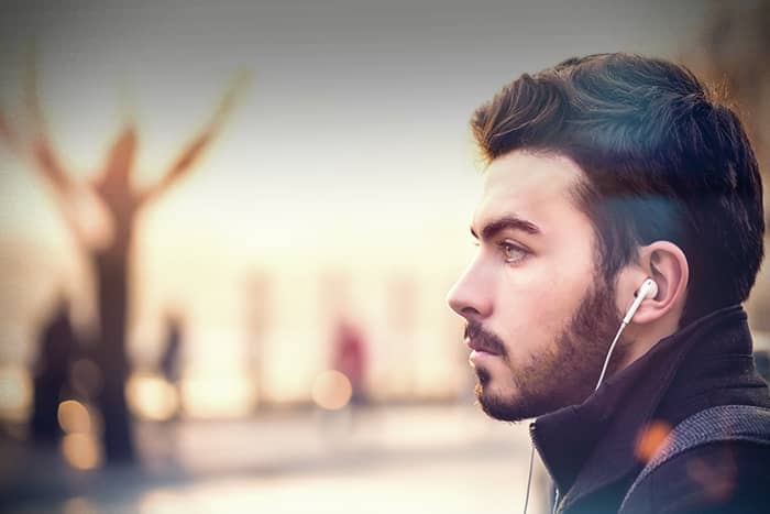 Ein junger Mann mit Bart hört Musik über Kopfhörer und blickt nachdenklich in die Ferne.
