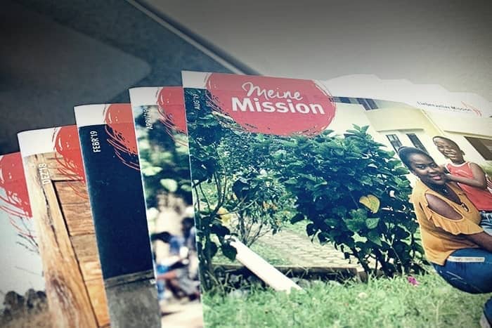 Mehrere Zeitschriften mit dem Titel "Meine Mission" sind aufgefächert und zeigen ein Foto von lächelnden Menschen und Grünpflanzen auf dem Titelbild.