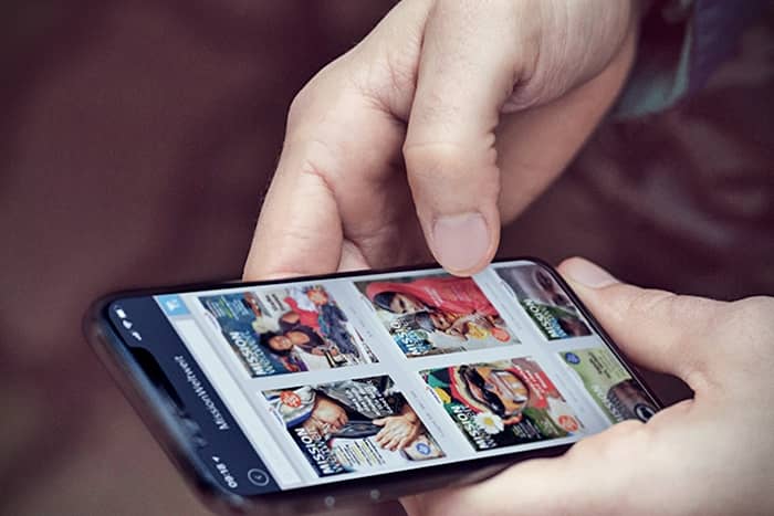 Eine Person hält ein Smartphone in der Hand und blättert auf dem Bildschirm durch ein Raster von Zeitschriftencovern.