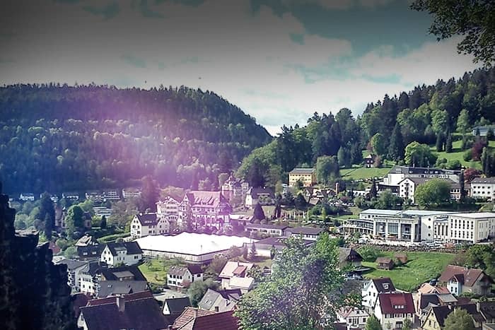 Eine kleine Stadt mit roten Dächern und Bäumen, eingebettet in ein grünes Tal, umgeben von bewaldeten Hügeln.