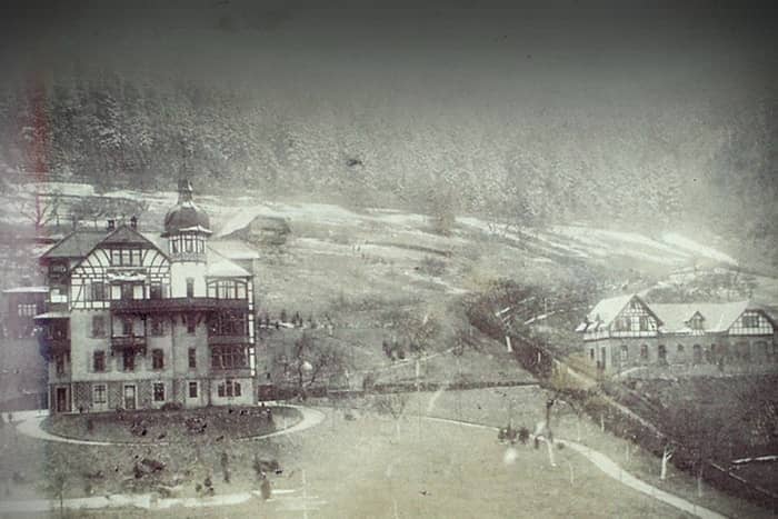 Alte Fotografie von zwei großen Gebäuden mit steilen Dächern in einer verschneiten Waldlandschaft.