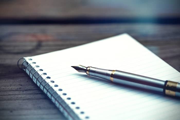 Ein Füllfederhalter liegt auf einem aufgeschlagenen Spiralnotizbuch mit linierten Seiten auf einer hölzernen Oberfläche.