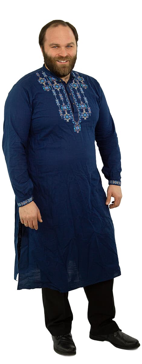 Mann, der eine blaue, traditionell bestickte Kurta über einer schwarzen Hose und Schuhen trägt, steht und lächelt in die Kamera.