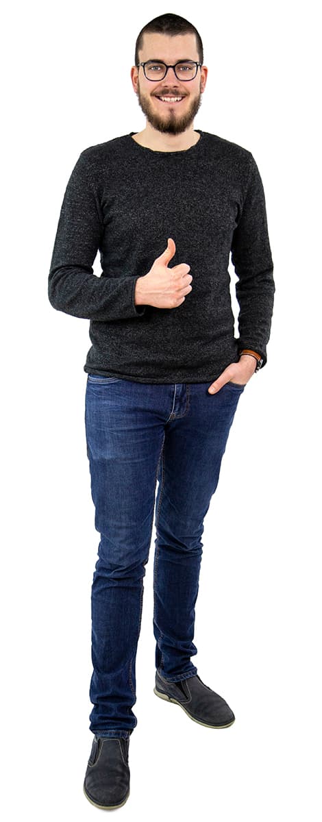 Mann mit Bart, der eine Brille, einen dunklen Pullover und Jeans trägt, lächelt und den Daumen nach oben streckt.