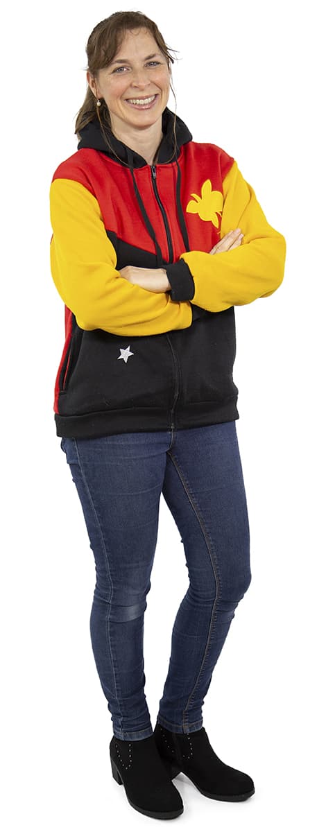 Lächelnde Frau mit verschränkten Armen, die eine bunte Jacke und blaue Jeans auf einem weißen Hintergrund trägt.