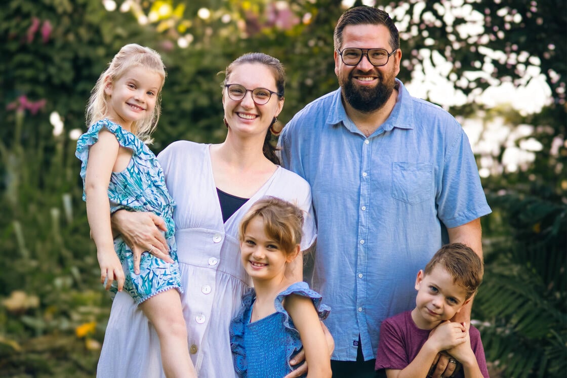 Eine lächelnde fünfköpfige Familie posiert im Freien vor einem grünen Hintergrund.