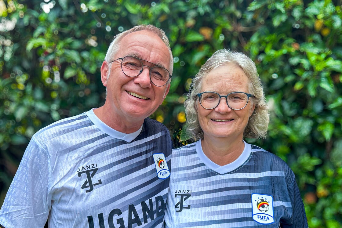 Ein lächelnder Mann und eine lächelnde Frau in passenden Uganda-Fußballtrikots, die im Freien vor einem Hintergrund aus üppigem Grün stehen.