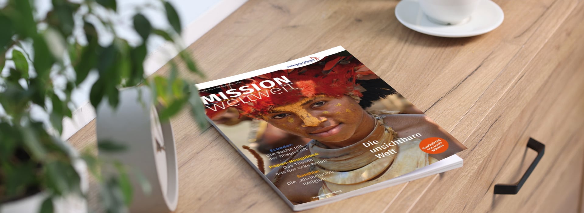 Eine Zeitschrift mit dem Titel „Mission weltweit“, auf deren Titelbild eine Frau in traditioneller Tracht und mit Gesichtsbemalung auf einem Holztisch neben einer Pflanze zu sehen ist.