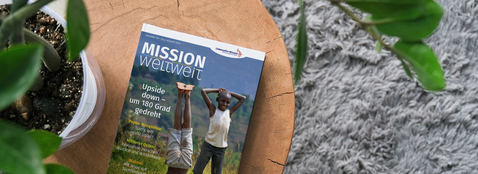 Die Zeitschrift „Mission weltweit“ liegt auf einem Holztisch neben einer Topfpflanze und einem grauen Teppich.