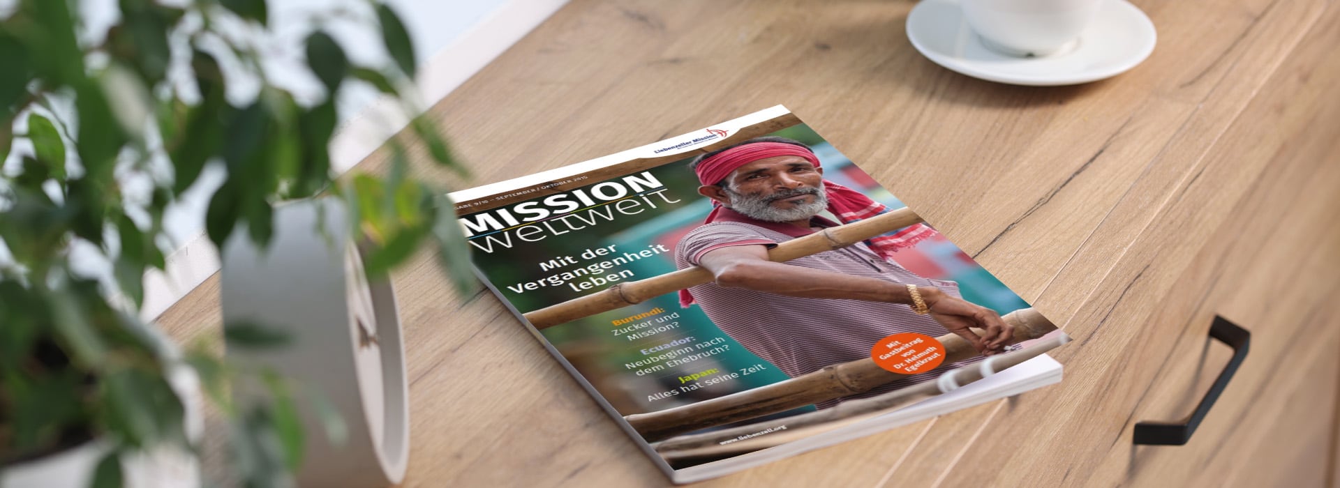 Ein Magazin mit dem Titel „Mission weltweit“, auf dem ein Mann mit rotem Turban auf einem Holztisch neben einer Pflanze und einer Kaffeetasse zu sehen ist.