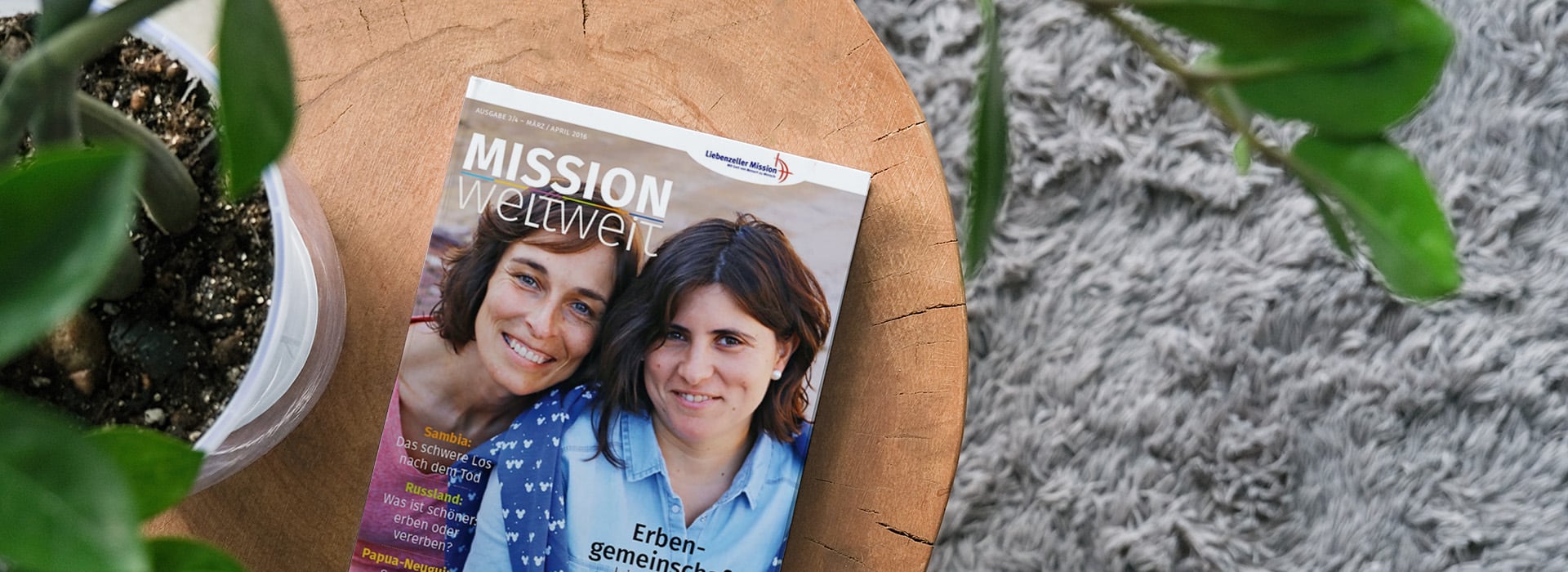 Eine Zeitschrift mit dem Titel „MISSION weltweit“, die auf einem Holztisch neben einer Zimmerpflanze und einem grauen Teppich liegt.