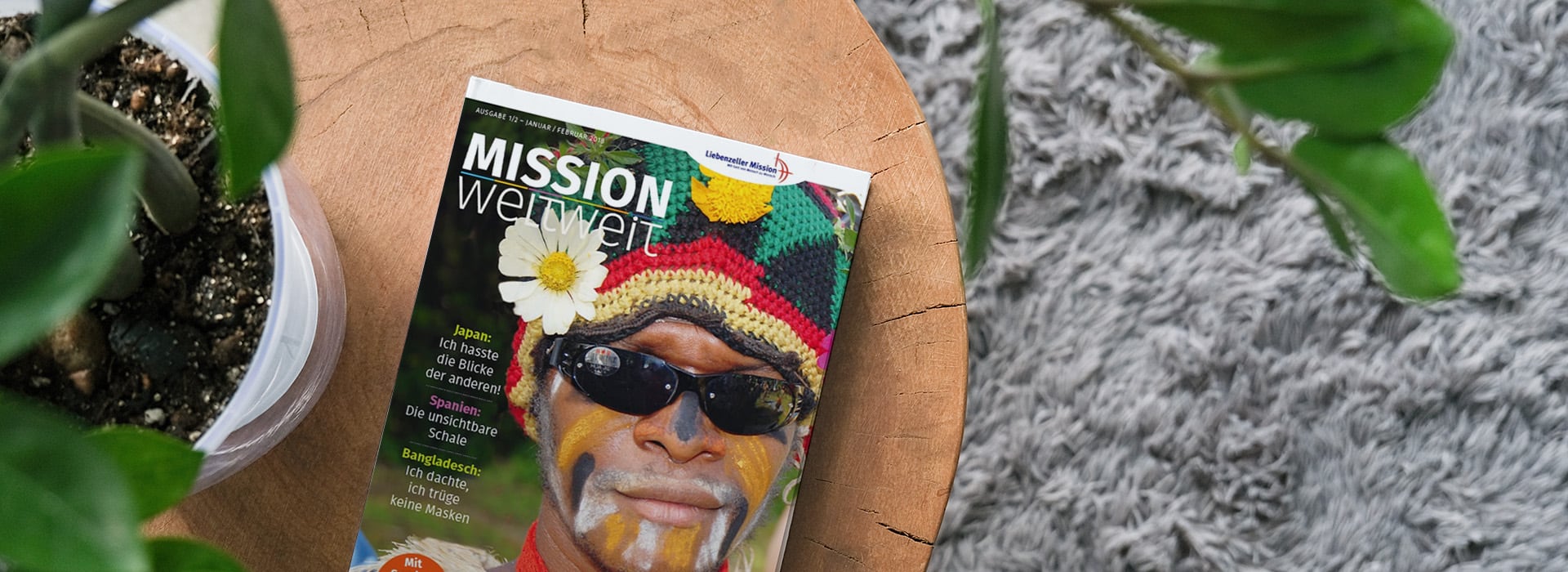 Eine Zeitschrift mit dem Titel „MISSION weltwei“, auf deren Titelbild eine Person mit bunter Kopfbedeckung und Sonnenbrille auf einem Holztisch neben Pflanzen zu sehen ist.