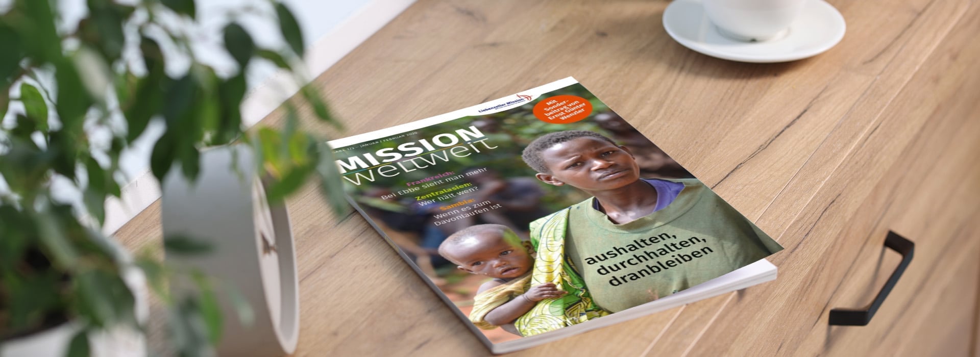 Eine Zeitschrift mit dem Titel „MISSION weltweit“, auf deren Titelseite ein Erwachsener und ein Kind auf einem Holztisch neben einer Pflanze und einer Tasse zu sehen sind.