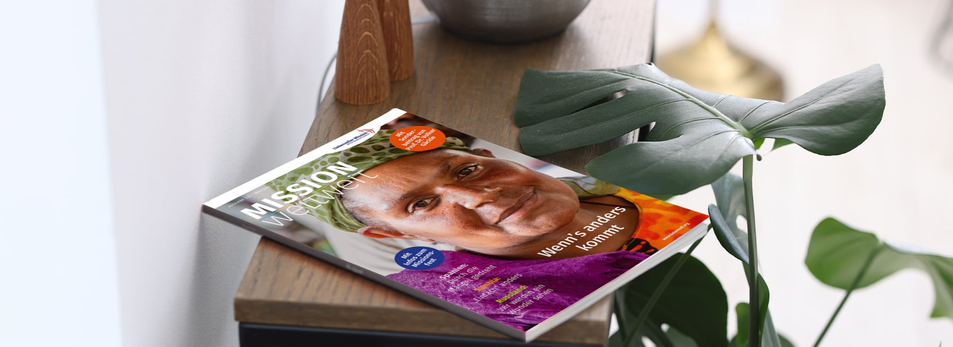Auf einem Holztisch neben einer grünen Pflanze liegt eine Zeitschrift, auf deren Titelseite eine Nahaufnahme einer lächelnden Person zu sehen ist.