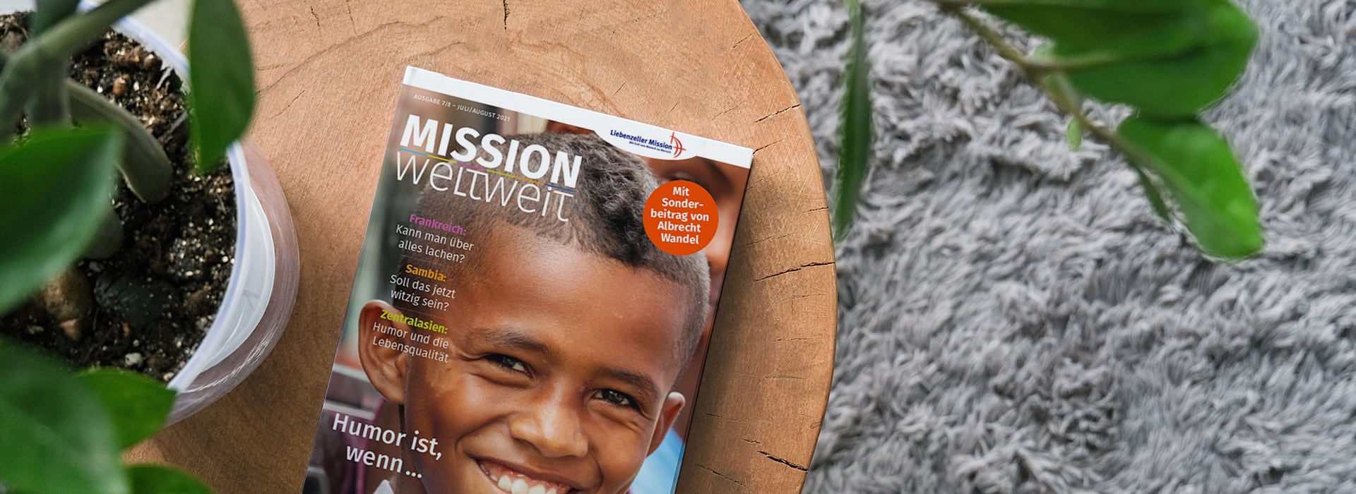 Eine Zeitschrift mit dem Titel „Mission weltweit“, auf deren Titelseite ein lächelnder Junge zu sehen ist, liegt auf einem Holztisch neben einigen Grünpflanzen.