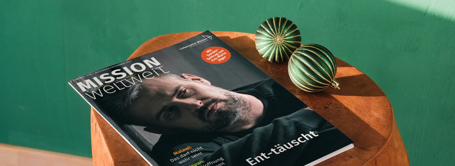 Auf einem Holzhocker neben zwei grünen Deko-Ornamenten liegt eine Zeitschrift mit dem Titel „MISSION weltweit“.