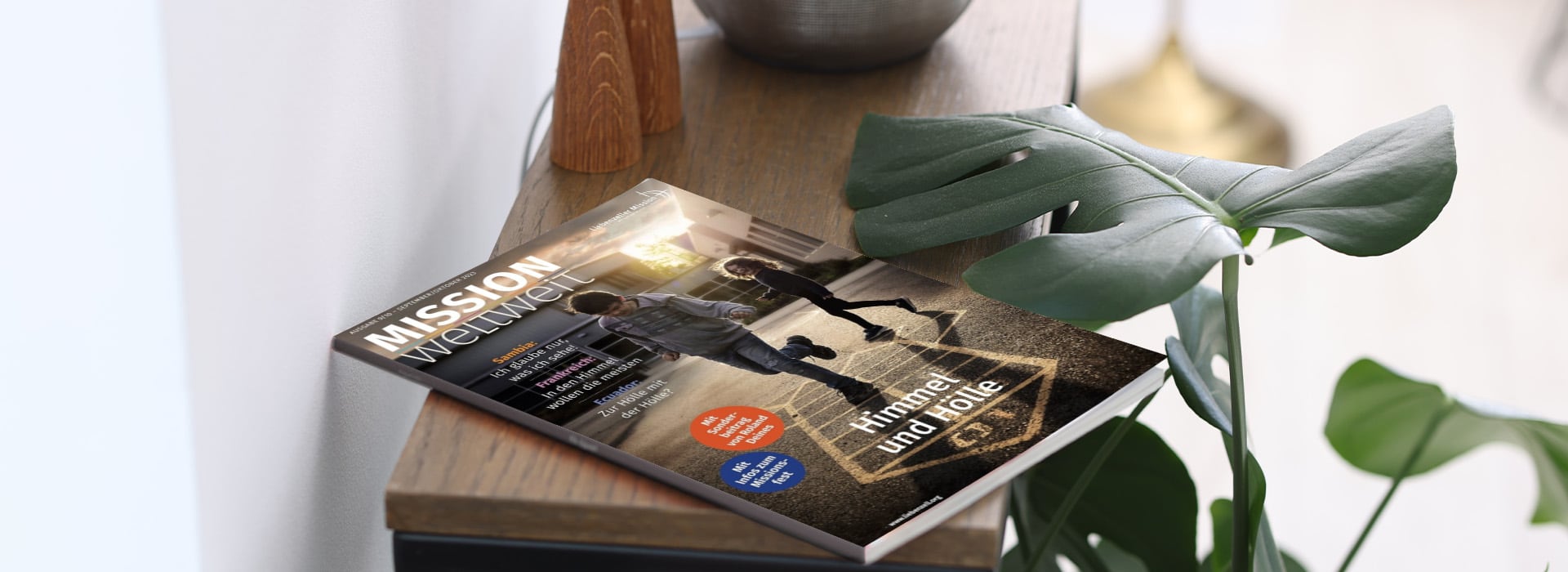 Die Zeitschrift „MISSION weltweit“ auf einem Holzregal neben einer Topfpflanze und einem Deko-Objekt.