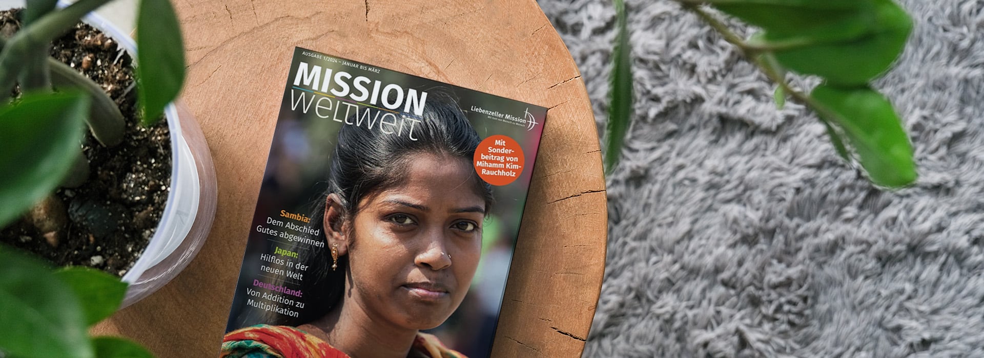 Eine Zeitschrift mit dem Titel „MISSION weltweit“, auf deren Titelseite eine Frau abgebildet ist, liegt auf einem Holztisch neben einer Topfpflanze.