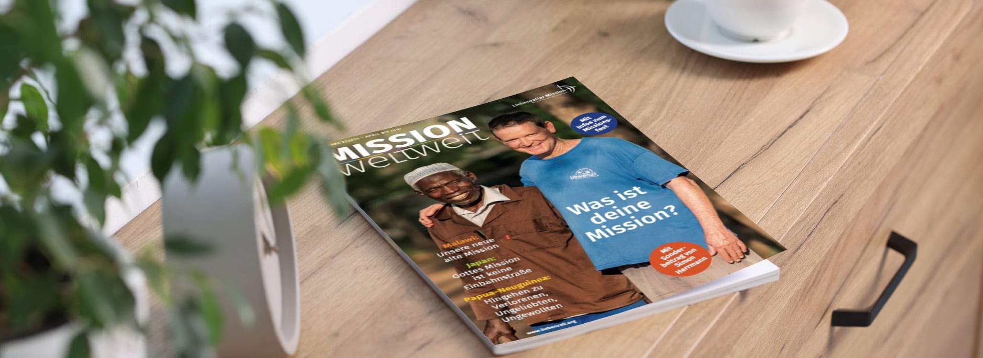 Die Zeitschrift „MISSION weltweit“ liegt auf einem Holztisch; darauf sind zwei Männer zu sehen, die lächelnd Arm in Arm gehen.