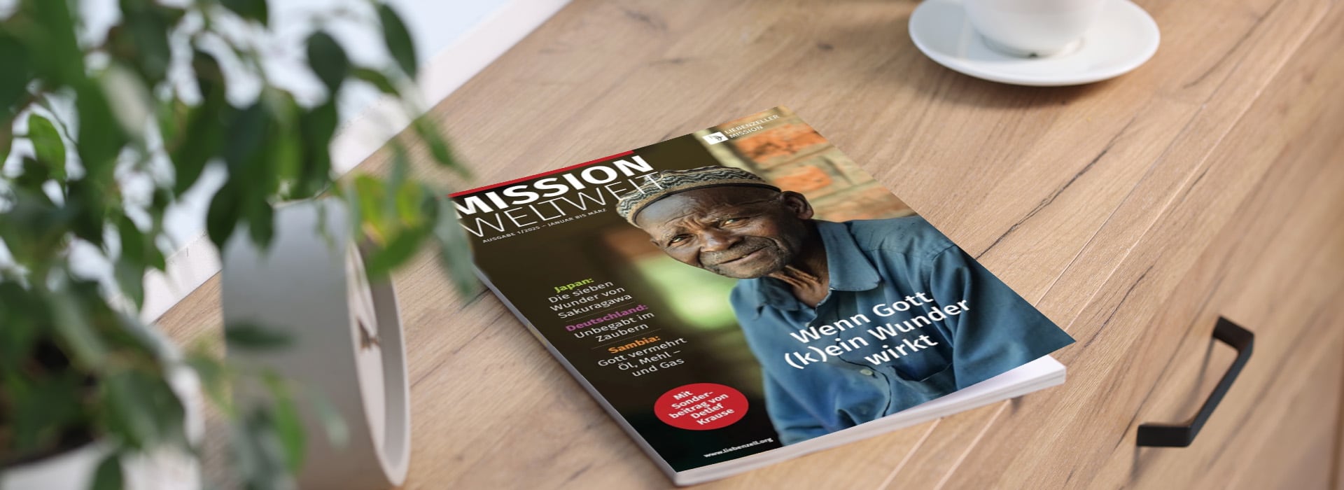 Auf einem Holztisch neben einer Pflanze und einer Tasse liegt eine Zeitschrift mit dem Titel „Mission weltweit“, auf deren Titelseite ein älterer Mann abgebildet ist.