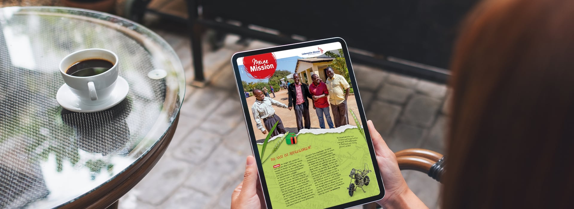 Eine Person sitzt mit einer Tasse Kaffee an einem Tisch und hält ein Tablet in der Hand, auf dem ein humanitärer Newsletter zu sehen ist.
