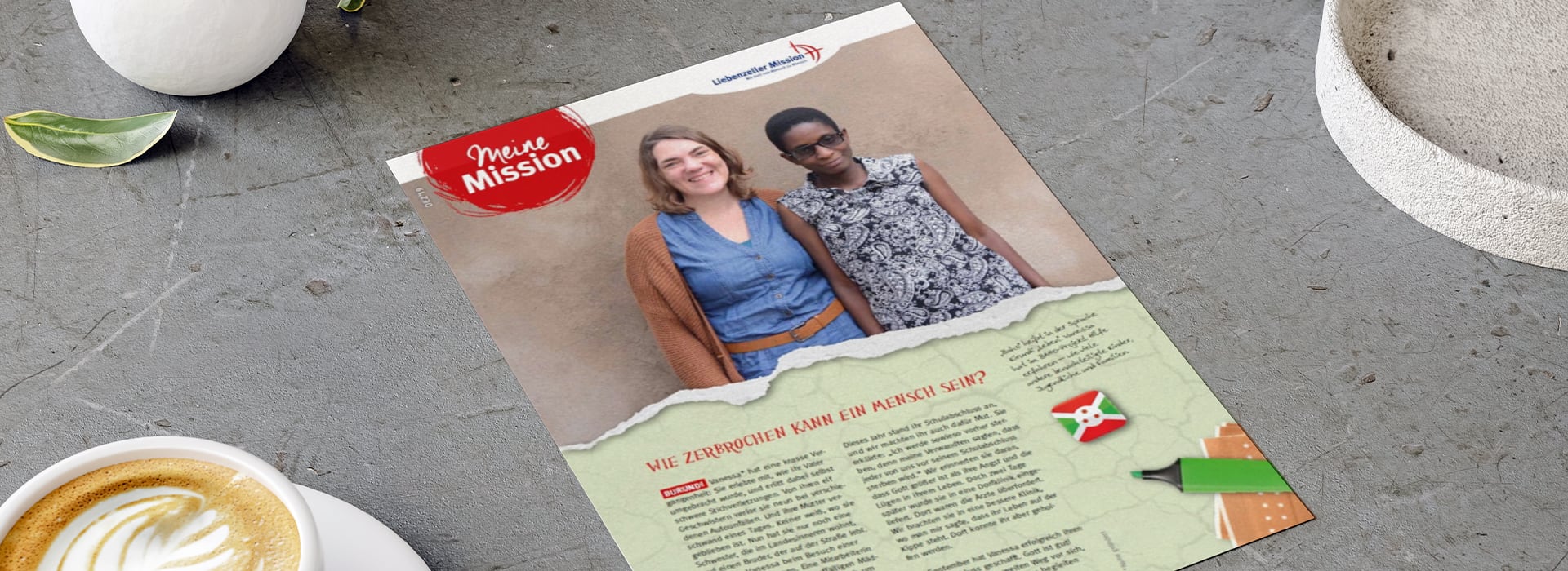 Auf einem Flyer, der auf einem Tisch liegt, sind zwei lächelnde Frauen zu sehen; im unteren Bereich befinden sich ein Text und die Flagge Burundis.