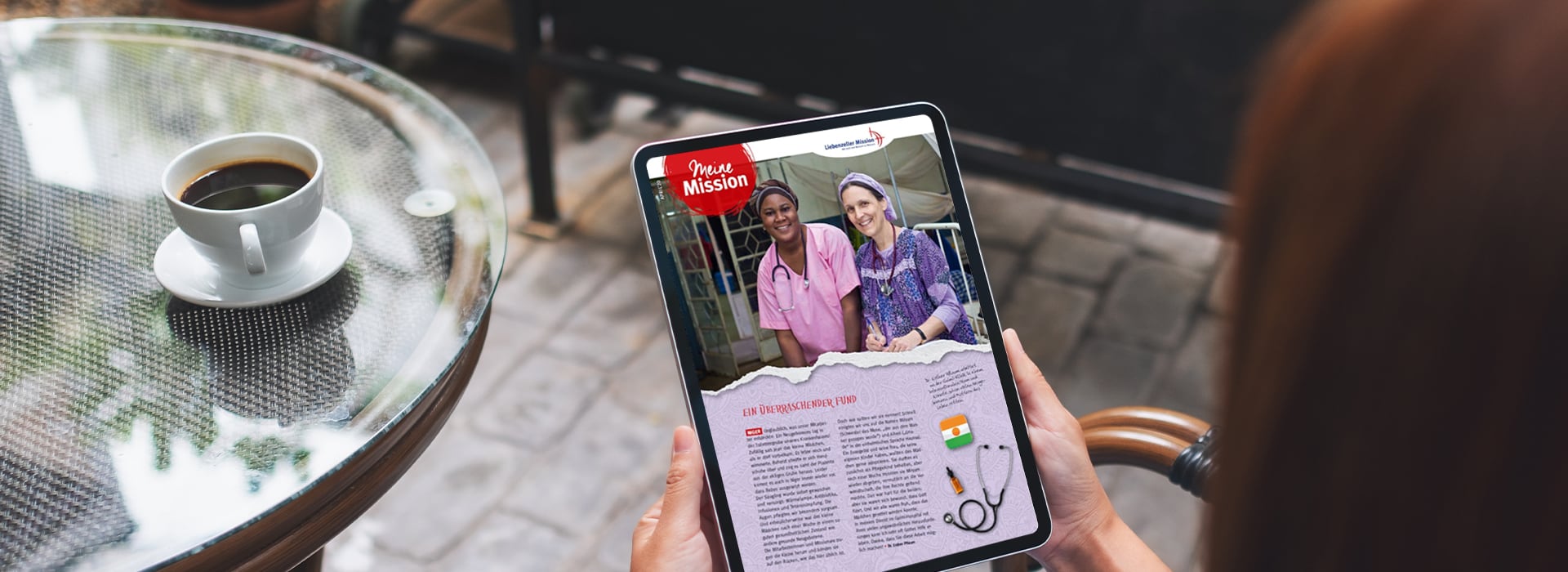 Eine Person hält ein Tablet in der Hand, auf dem ein Artikel mit zwei Frauen in medizinischer Kleidung zu sehen ist, daneben steht eine Tasse Kaffee auf einem Glastisch.
